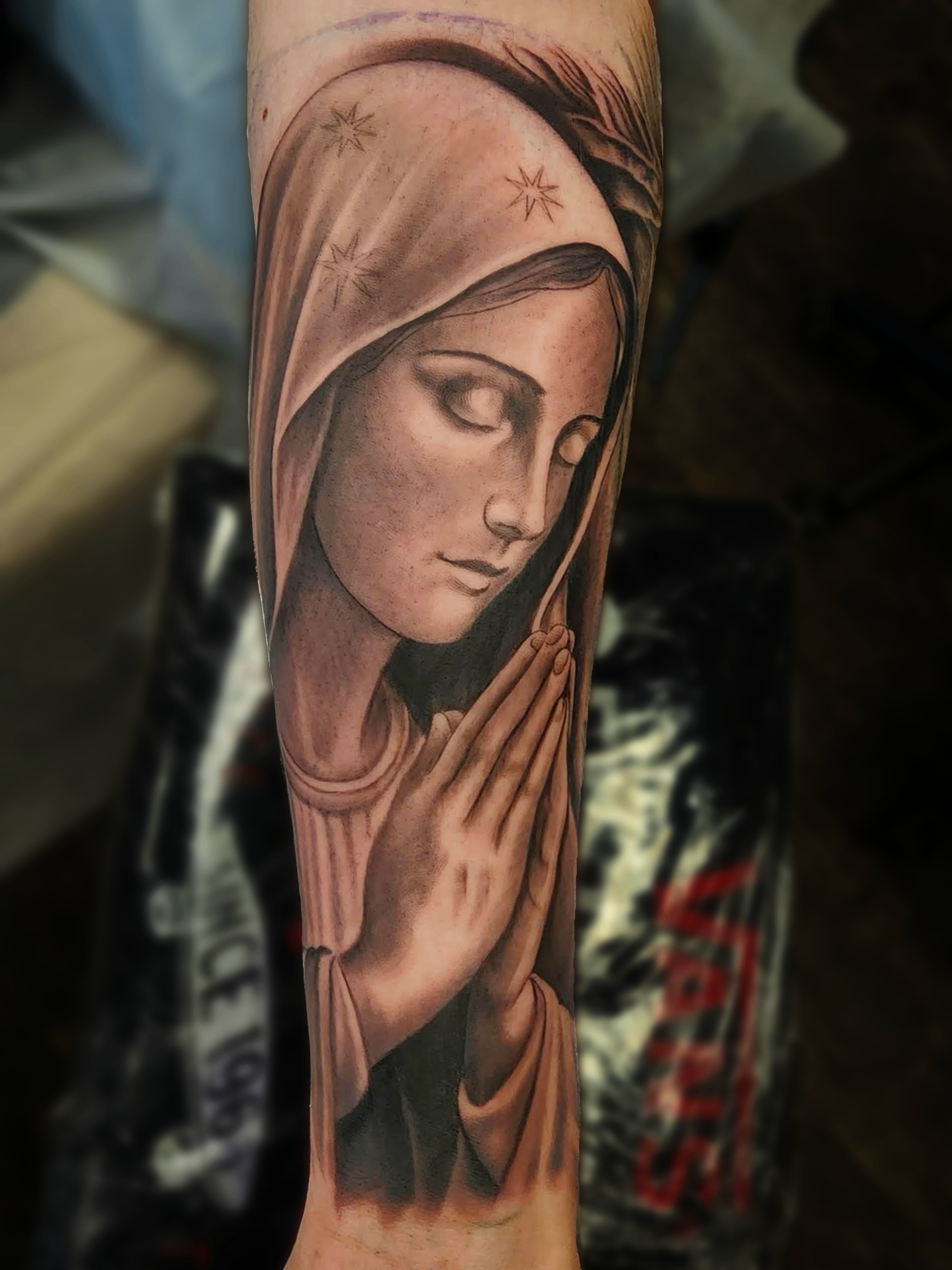 Black and grey realism forearm tattoo of the Virgin Mary in prayer beneath a starred veil