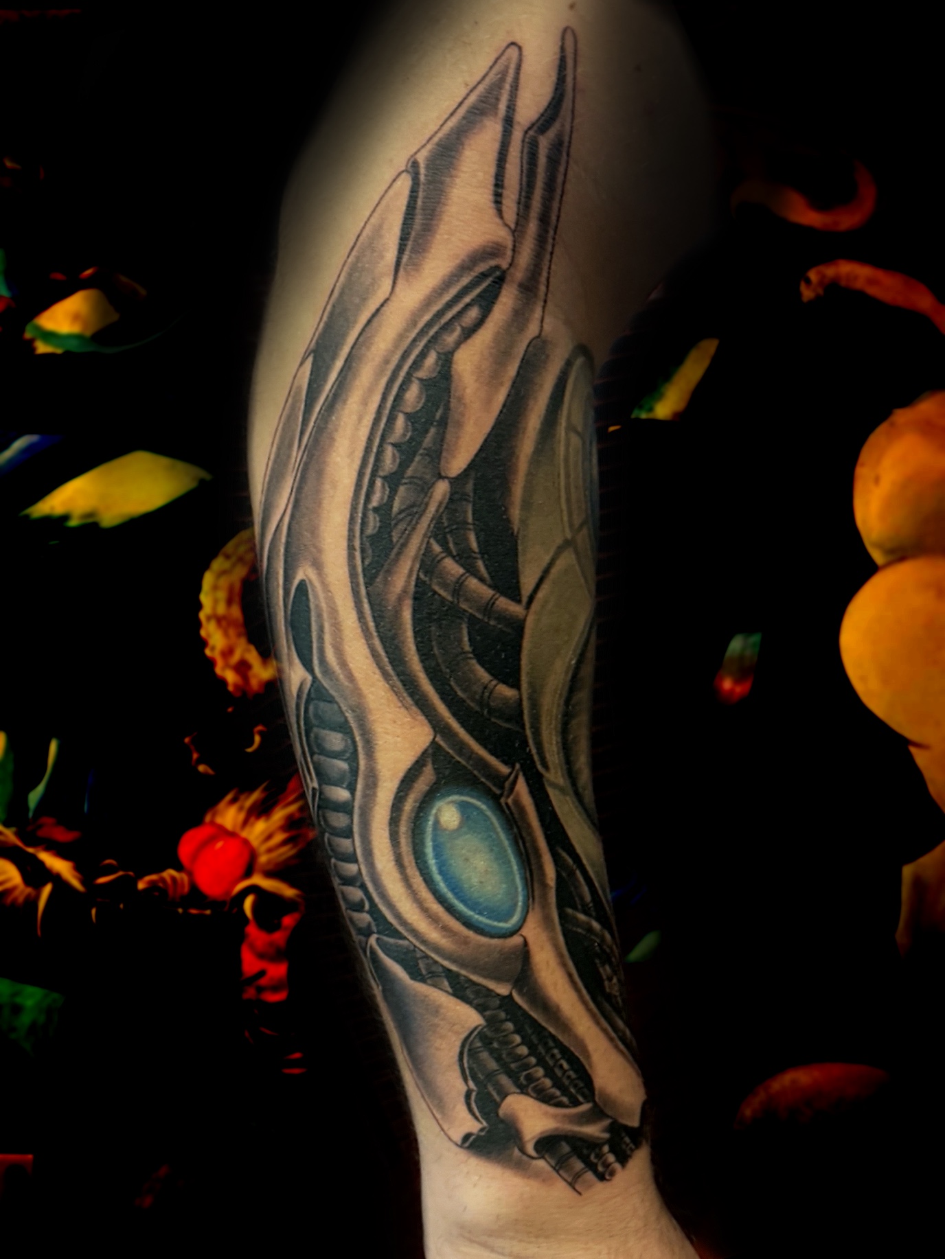 Biomechanical forearm tattoo with bone-like plating surrounding a glowing blue orb