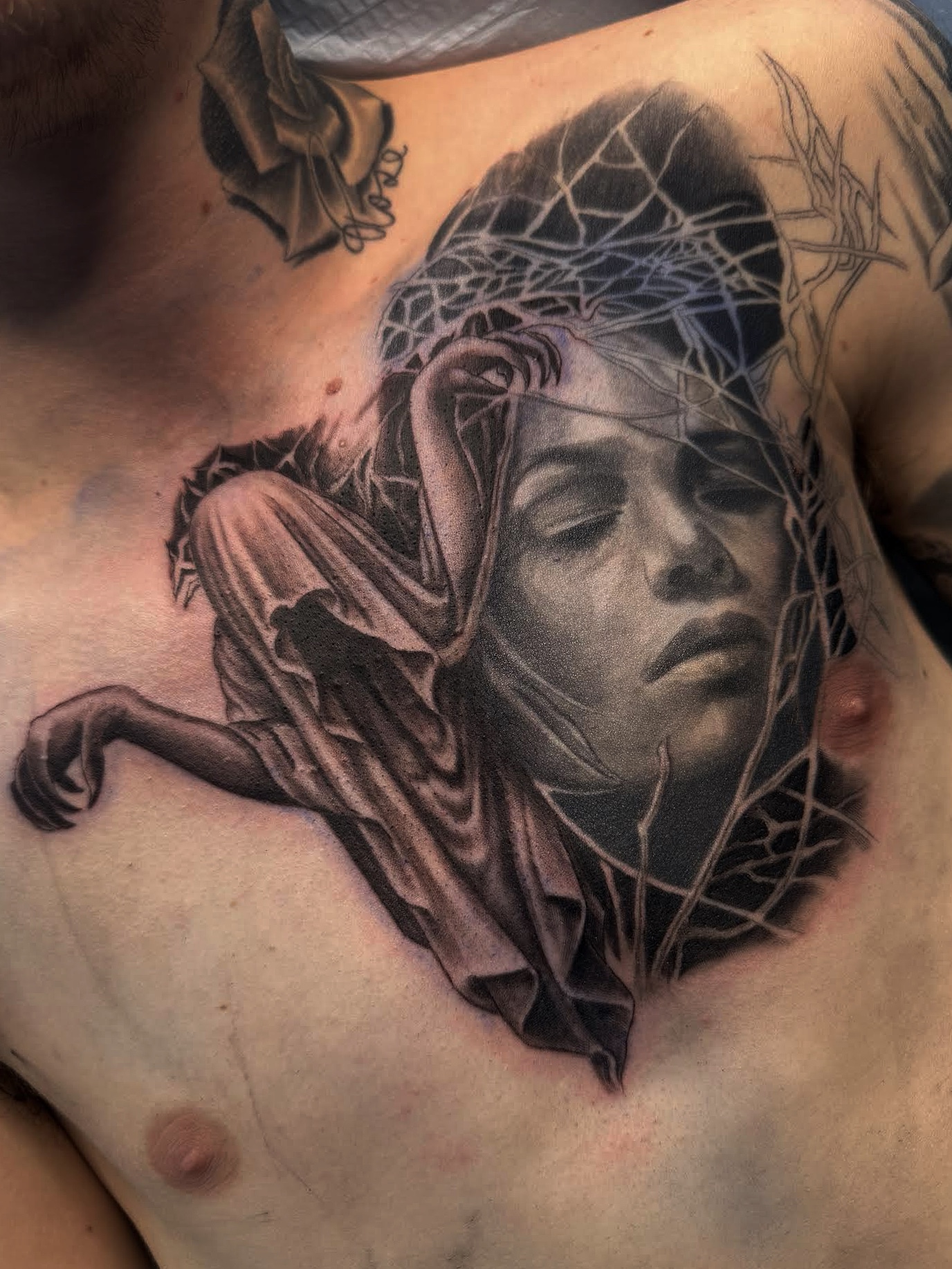 Black and grey realism chest tattoo of a sorrowful woman's face wrapped in a crown of thorns