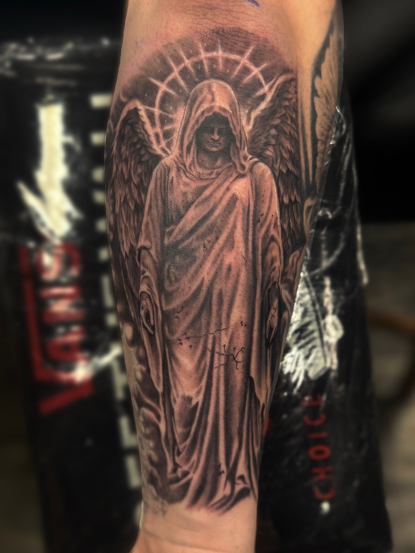 Black and grey realism forearm tattoo of a hooded angel statue with a radiant halo