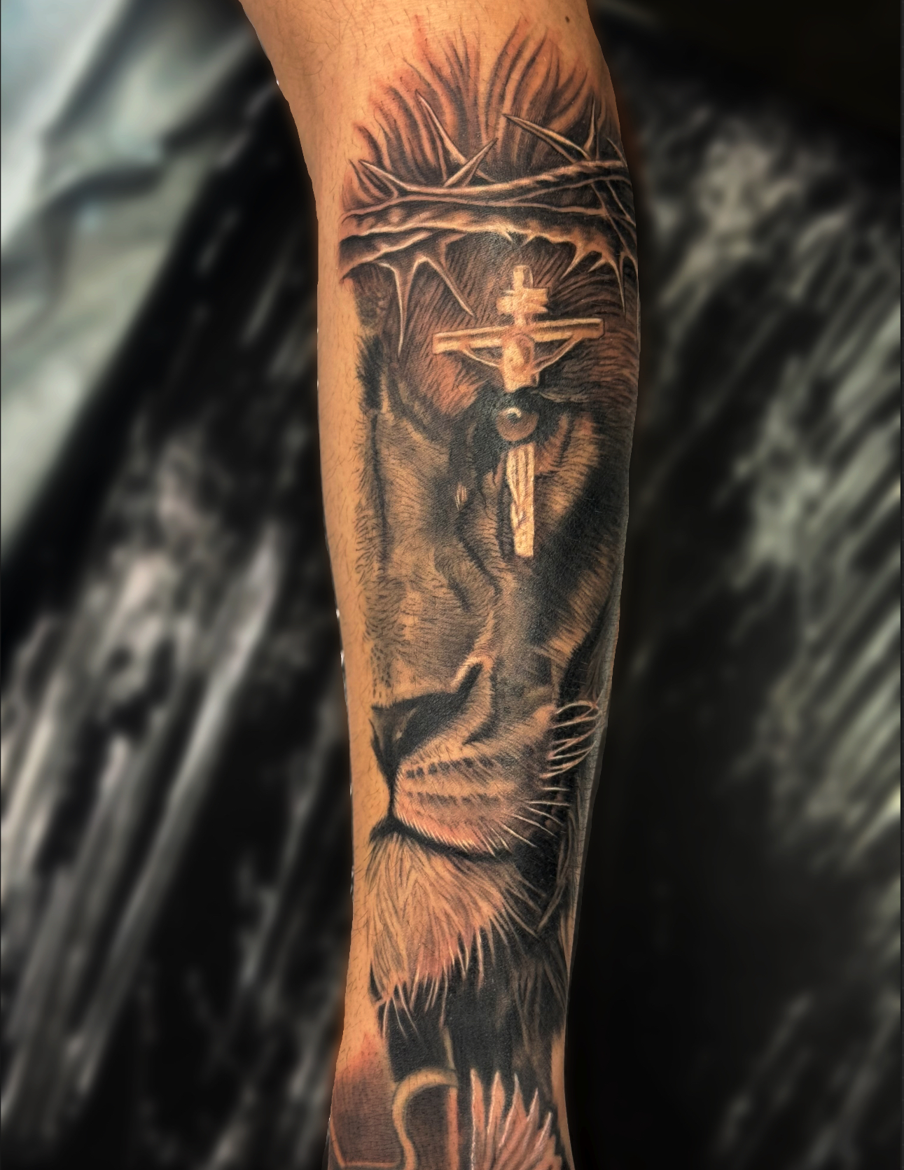 Black and grey realism forearm sleeve of a lion's face wearing a crown of thorns with a crucifix