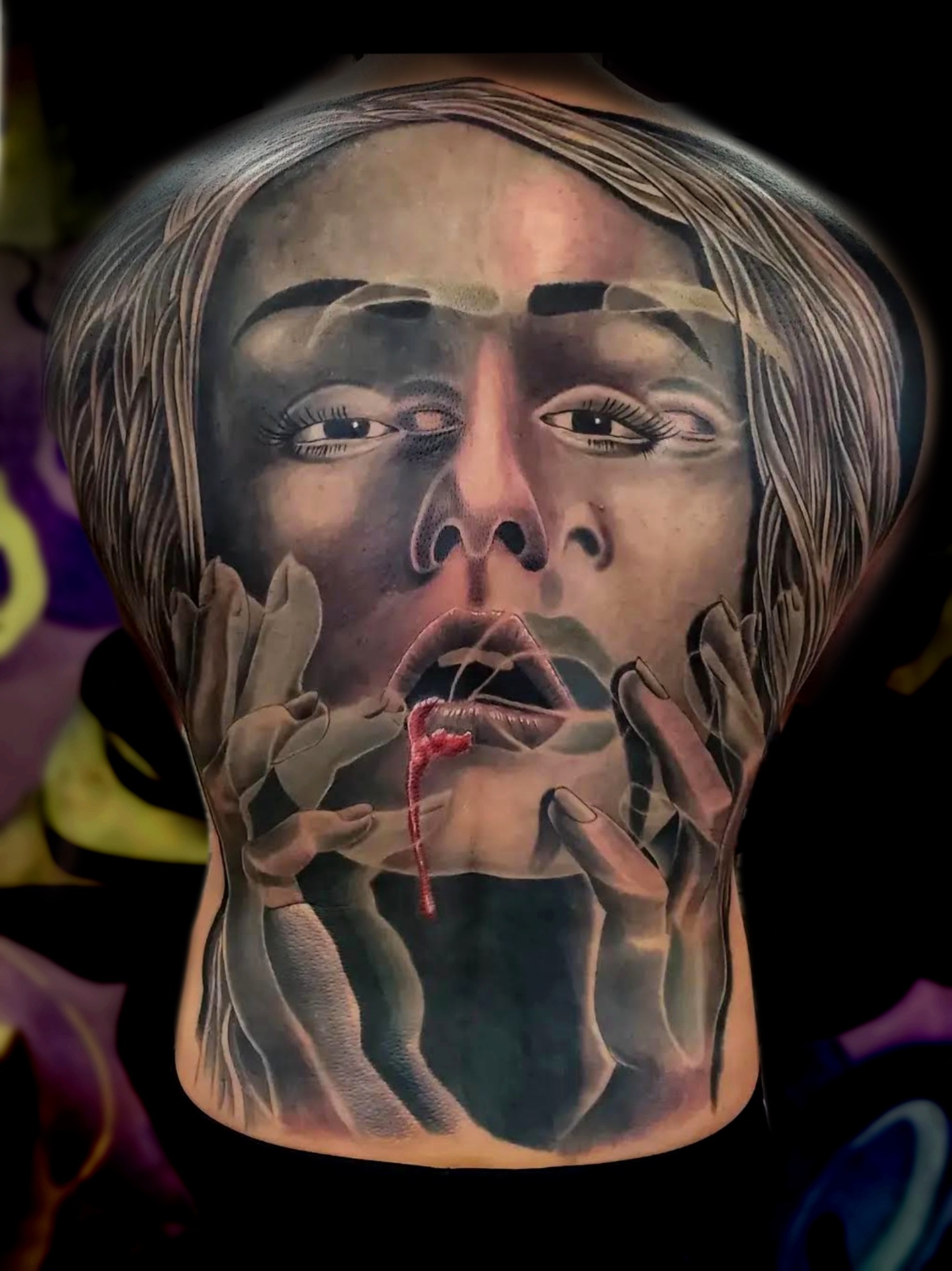 Colour realism back tattoo of a woman's face with hands reaching over her mouth and a red drip