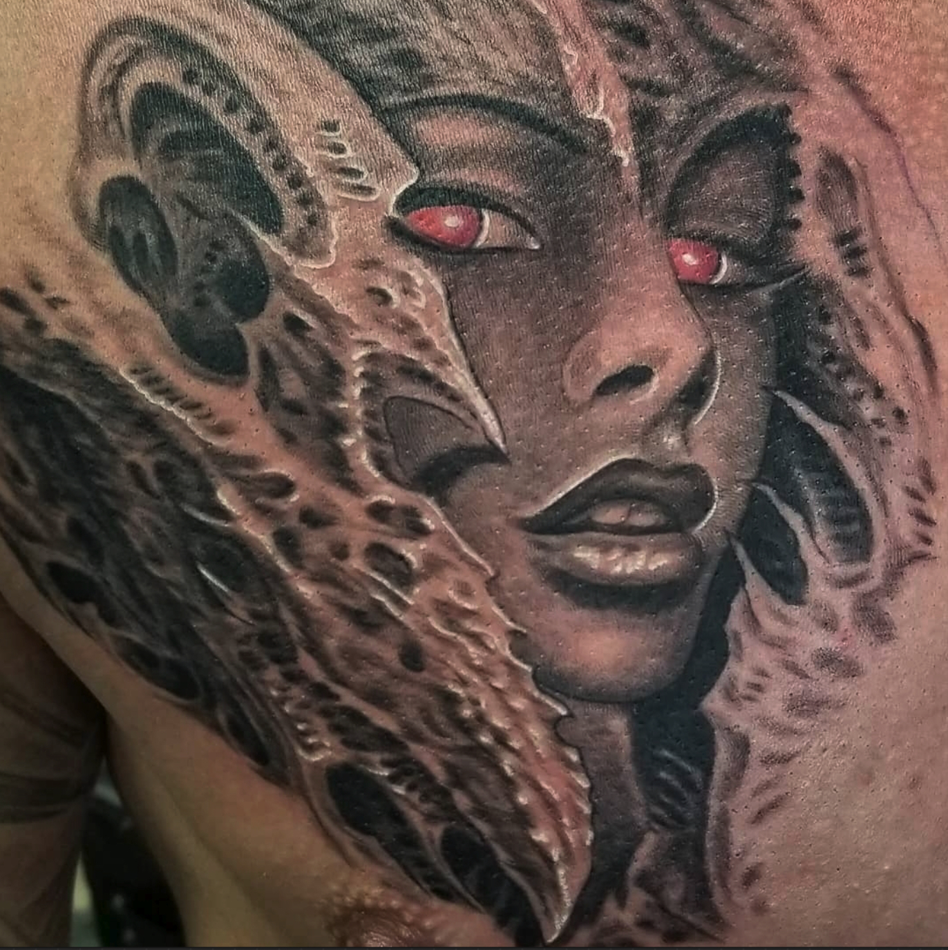 Black and grey biomechanical chest tattoo of a woman's face with red eyes emerging from alien armour
