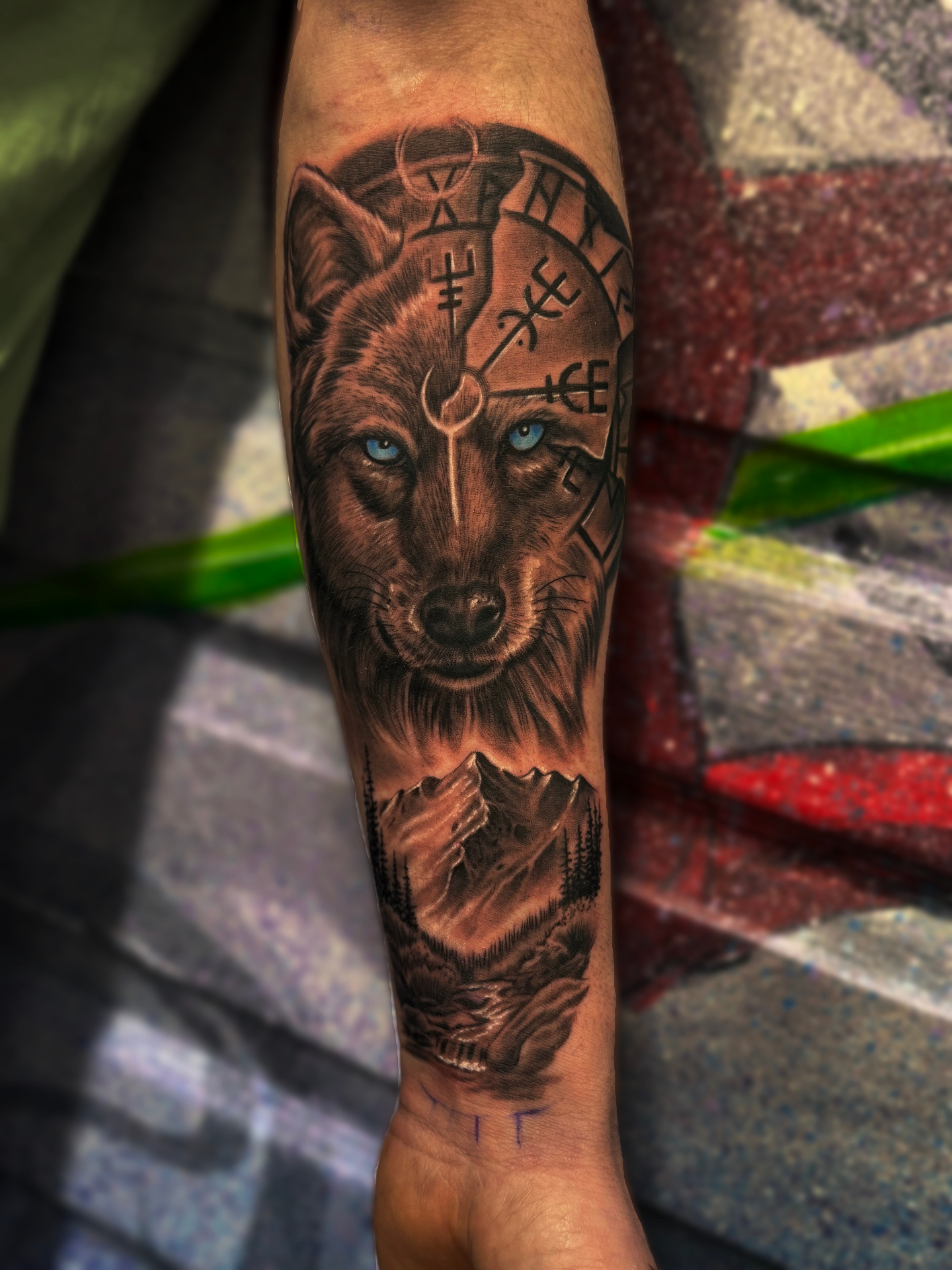Colour realism forearm sleeve of a wolf with piercing blue eyes, Norse runes, and mountain landscape